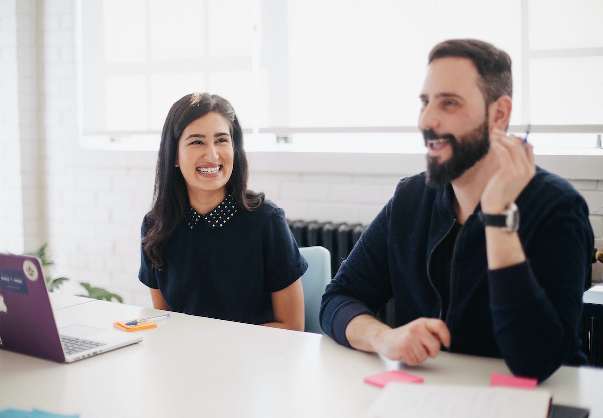 A Woman Smiles While Sitting Next to a Speaking Man in a Meeting Salsify Ecommerce Team Job Description Templates